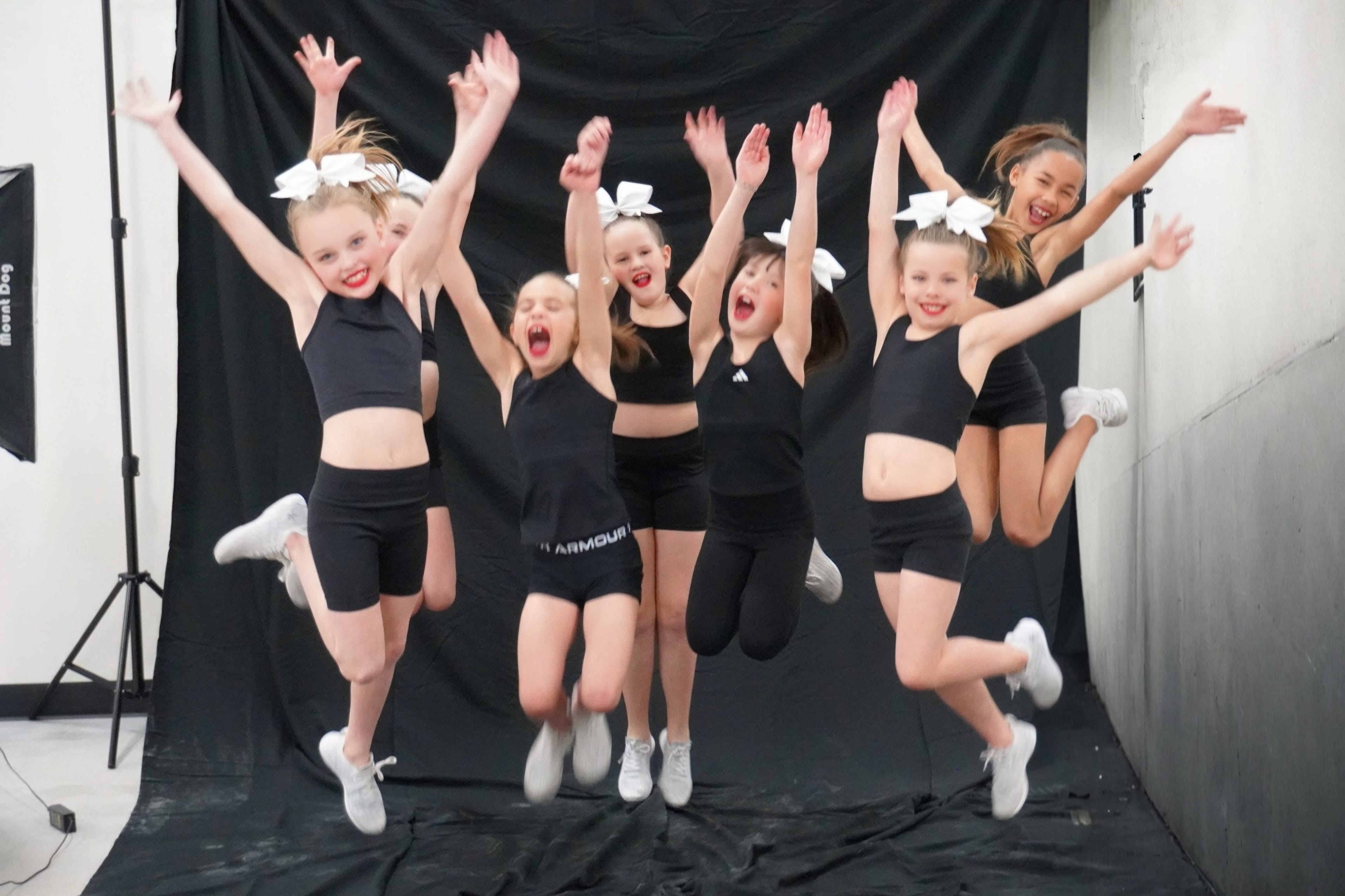 Group of excited dancers in black athletic wear jumping with arms raised